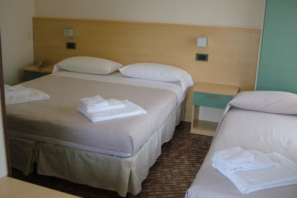 Une chambre d’hôtel avec un lit double, deux lits simples, une table de chevet avec un téléphone et une autre table de chevet avec une lampe.