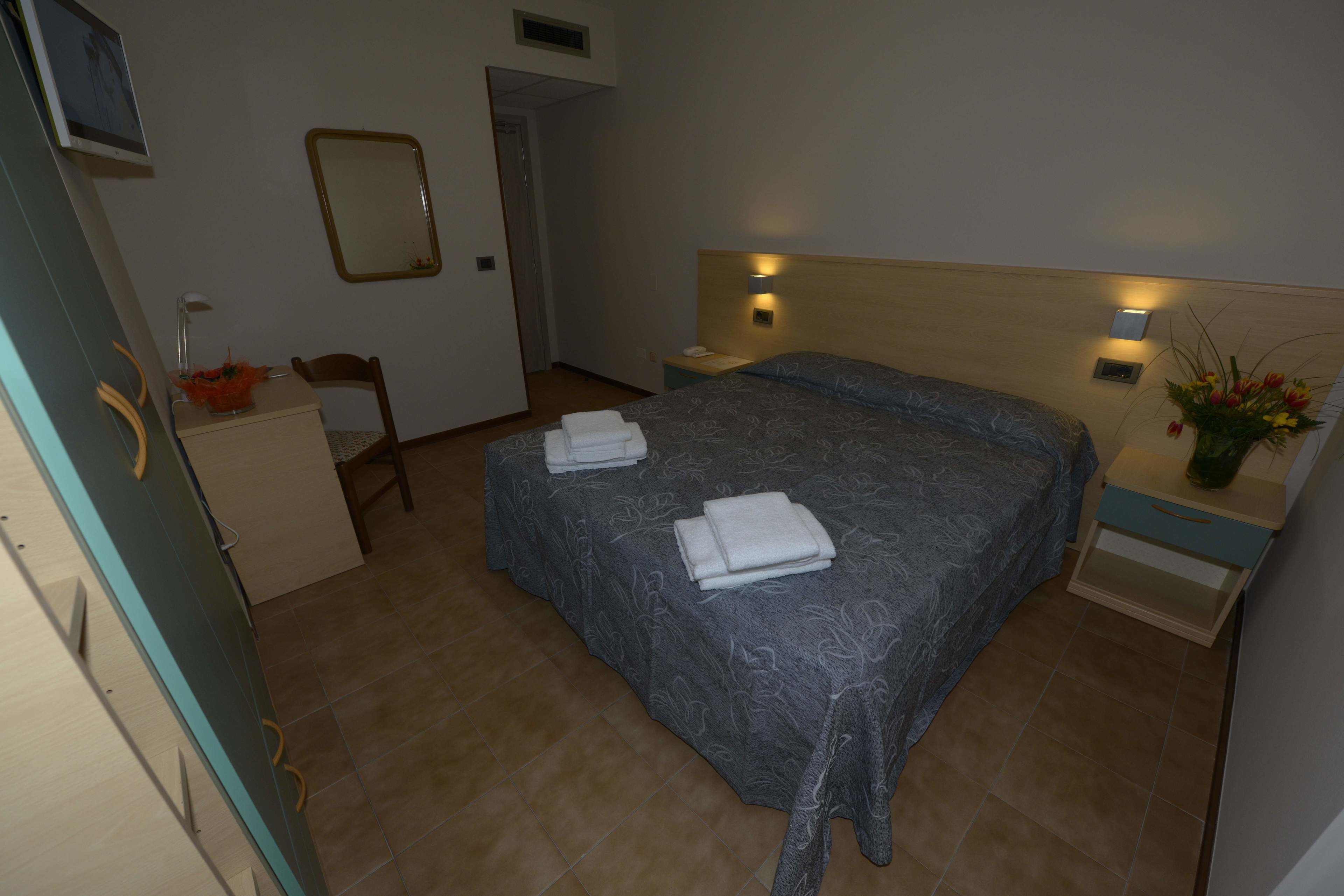 A bedroom with a bed, a nightstand, a chair, a dresser, a mirror, and a wall-mounted light fixture.