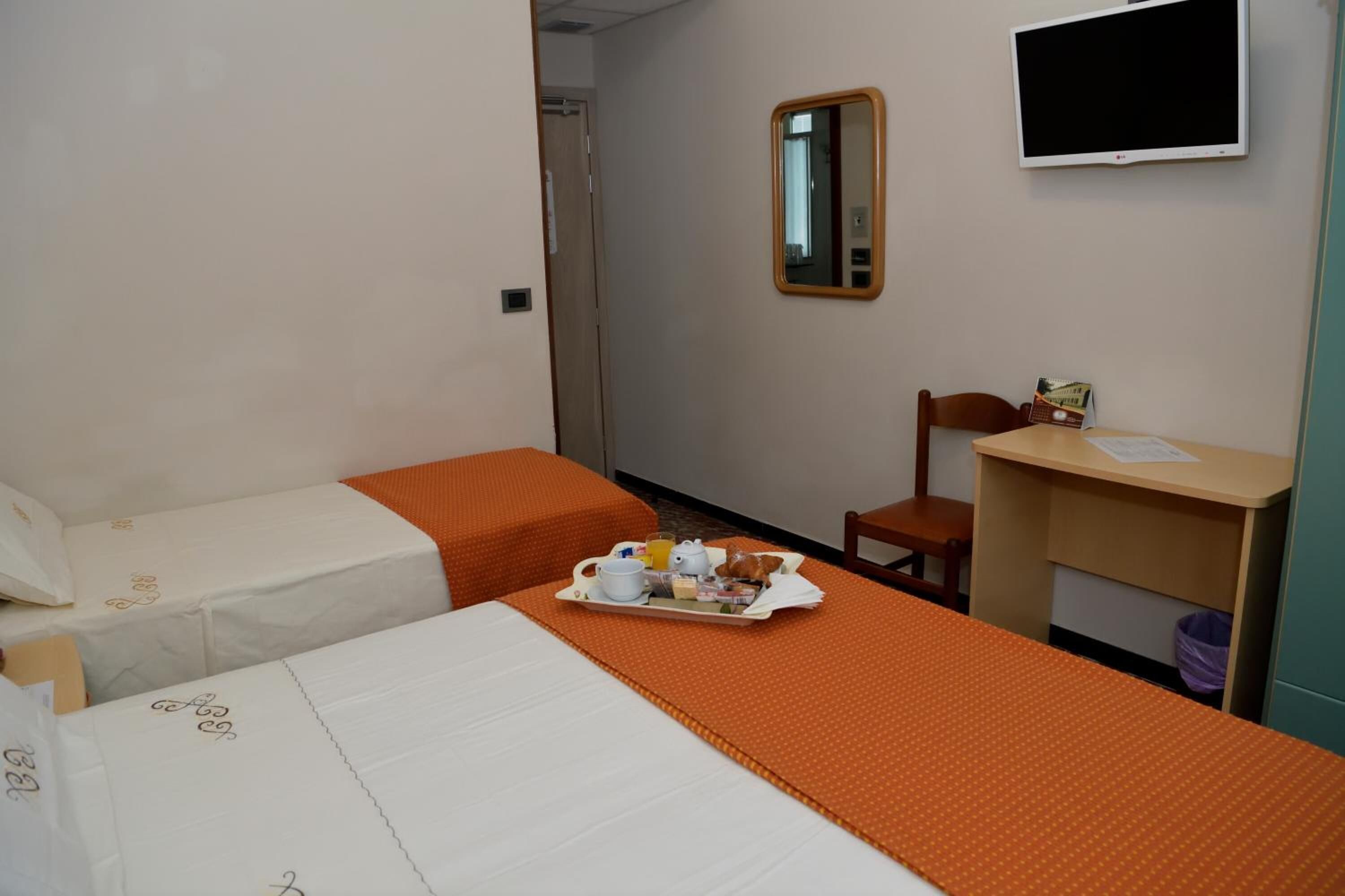 A hotel room with two beds, a desk with a chair, a television, and a tray with breakfast items.