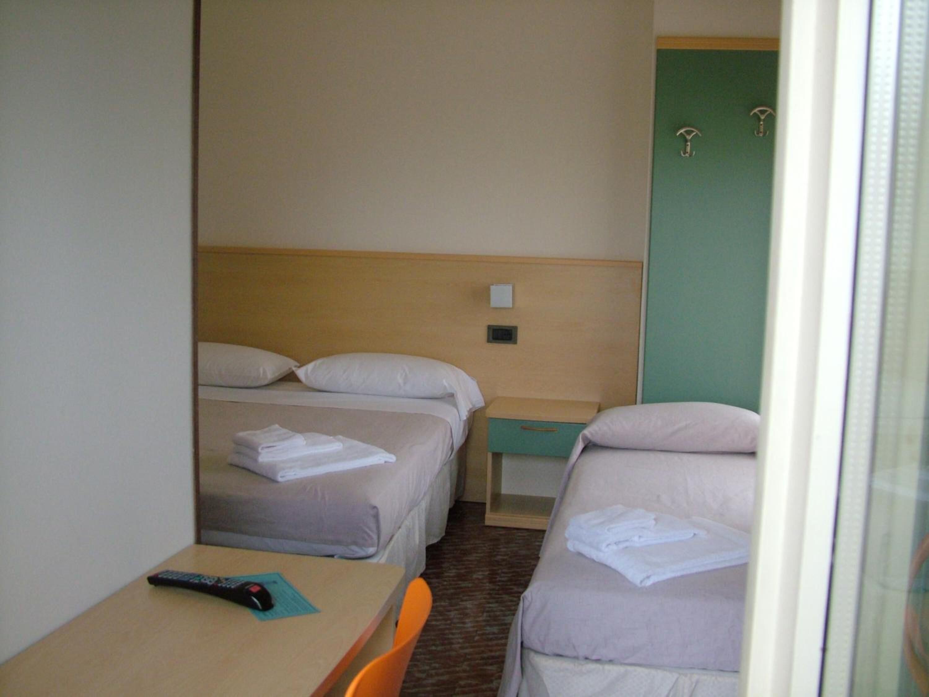 Une chambre d’hôtel avec deux lits, une petite table avec une télécommande et une porte verte.