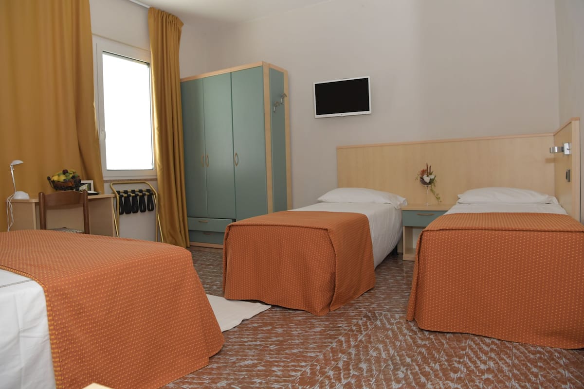 Une chambre d’hôtel avec deux lits, une télévision, une armoire et un bureau avec une lampe.