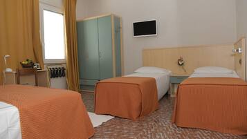 Ein Hotelzimmer mit zwei Betten, einem Fernseher, einem Kleiderschrank und einem Schreibtisch mit einer Lampe.