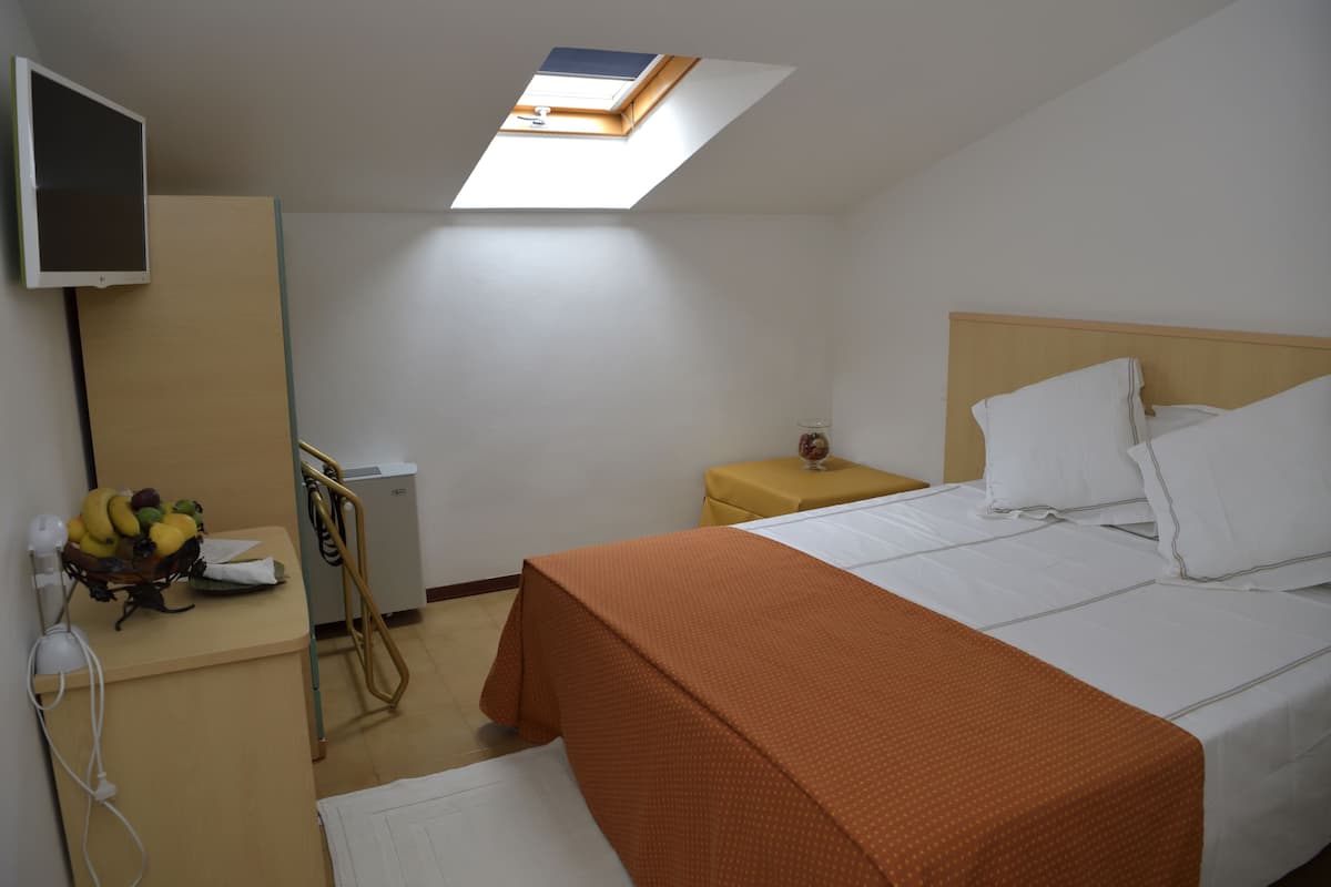 Une chambre d’hôtel avec un lit, un bureau avec un ordinateur, une petite table avec un vase et un panier de fruits.