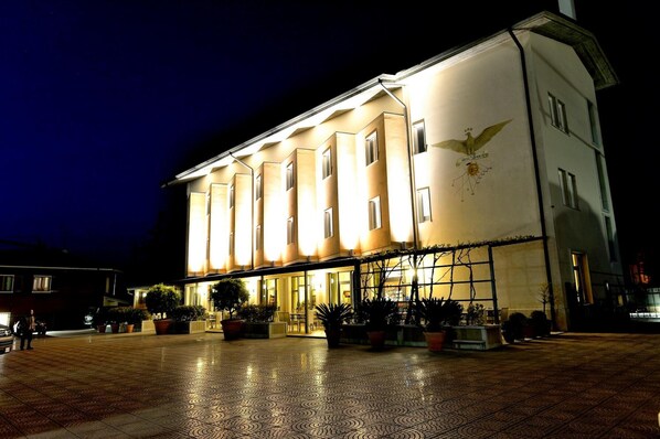 A large building with multiple windows and a central entrance, surrounded by potted plants and a tiled courtyard.