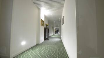 A narrow hallway with white walls and a green patterned carpet.