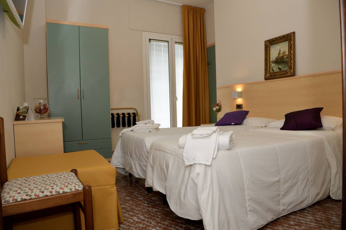 Une chambre d’hôtel avec deux lits, un bureau, une chaise et une armoire.