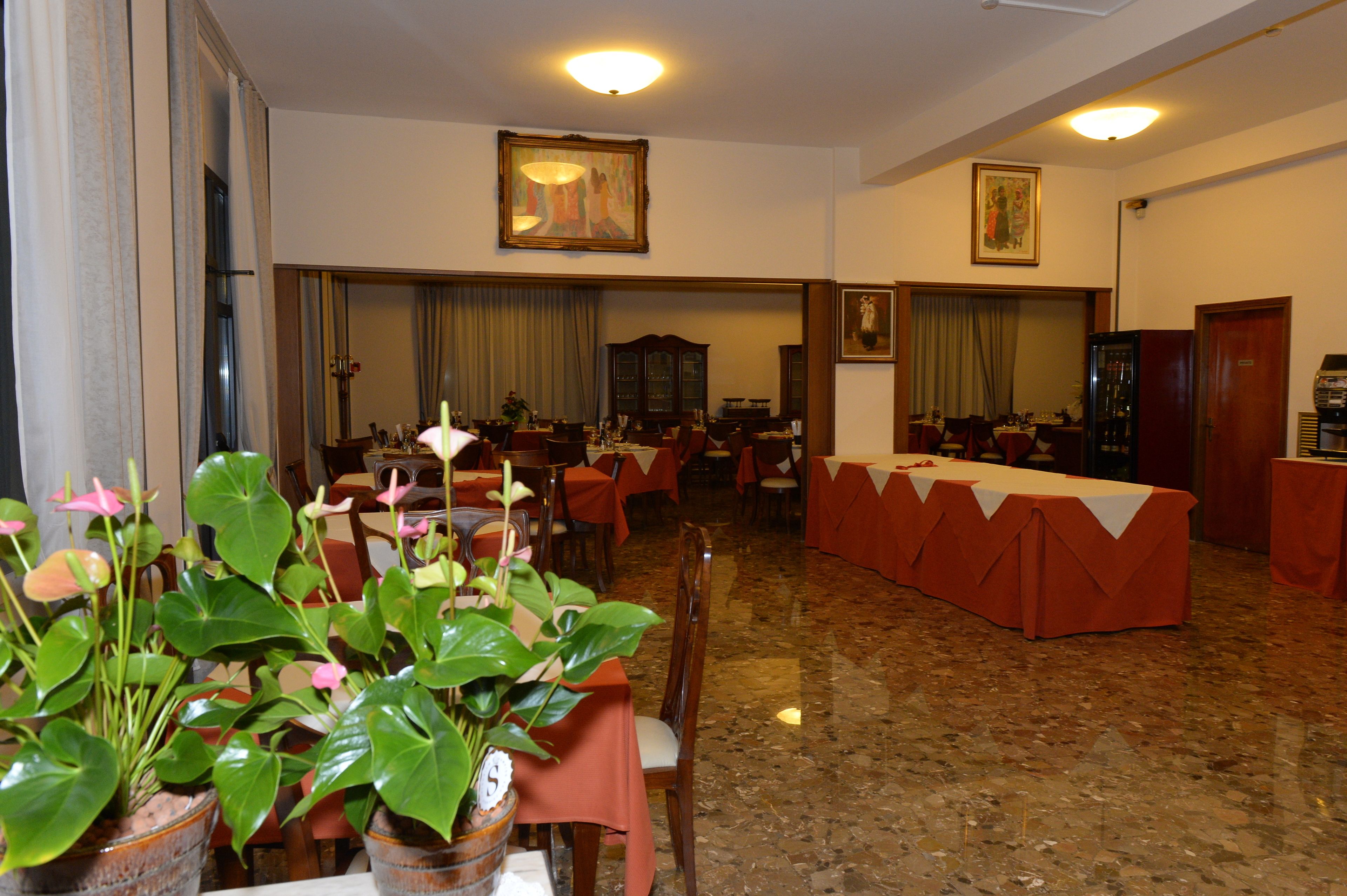 Une salle à manger d’hôtel avec des tables dressées pour le repas, des plantes en pot et des œuvres d’art accrochées aux murs.