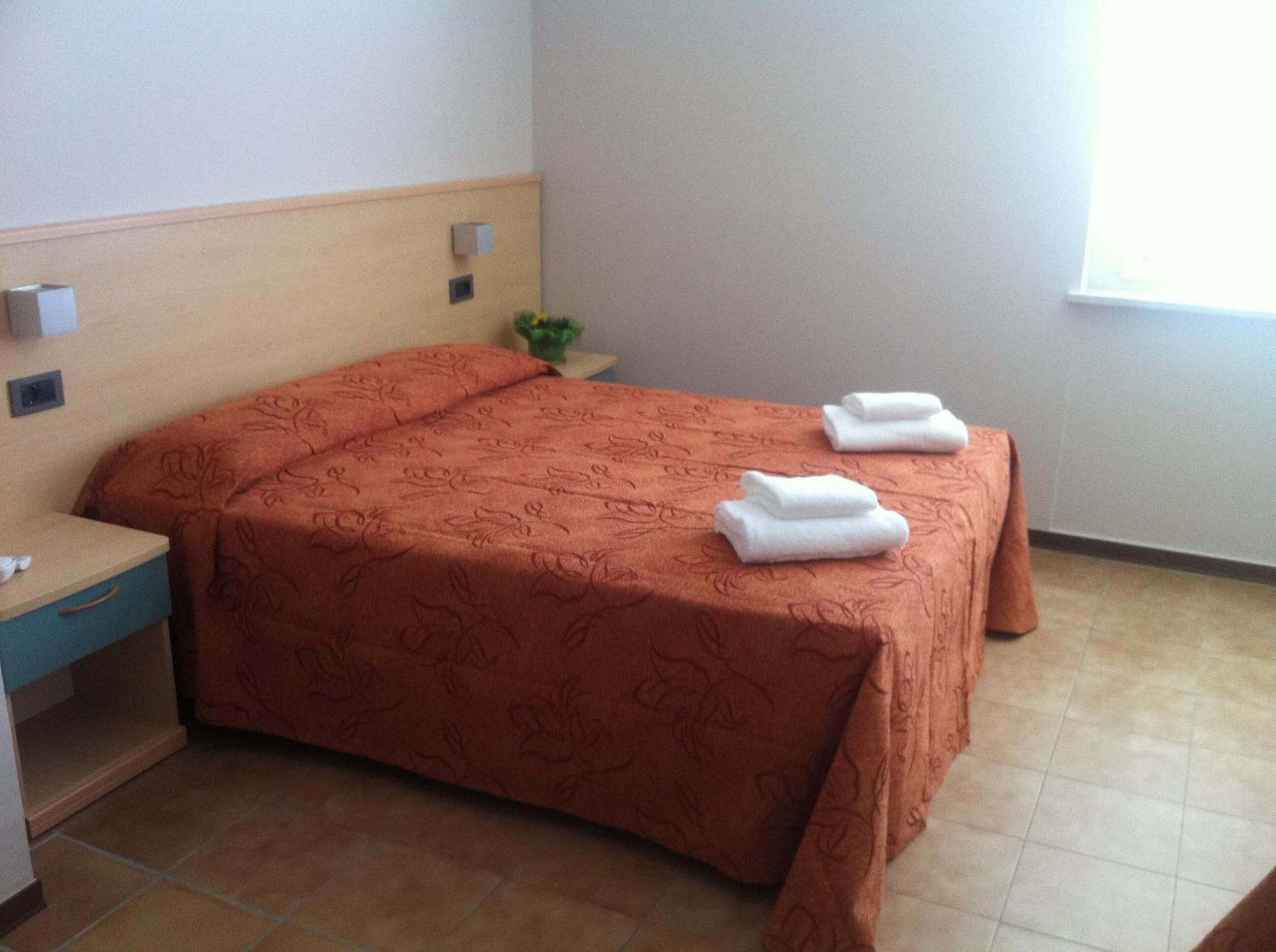 Una habitación de hotel con una cama, una mesita de noche, una planta pequeña y una ventana.