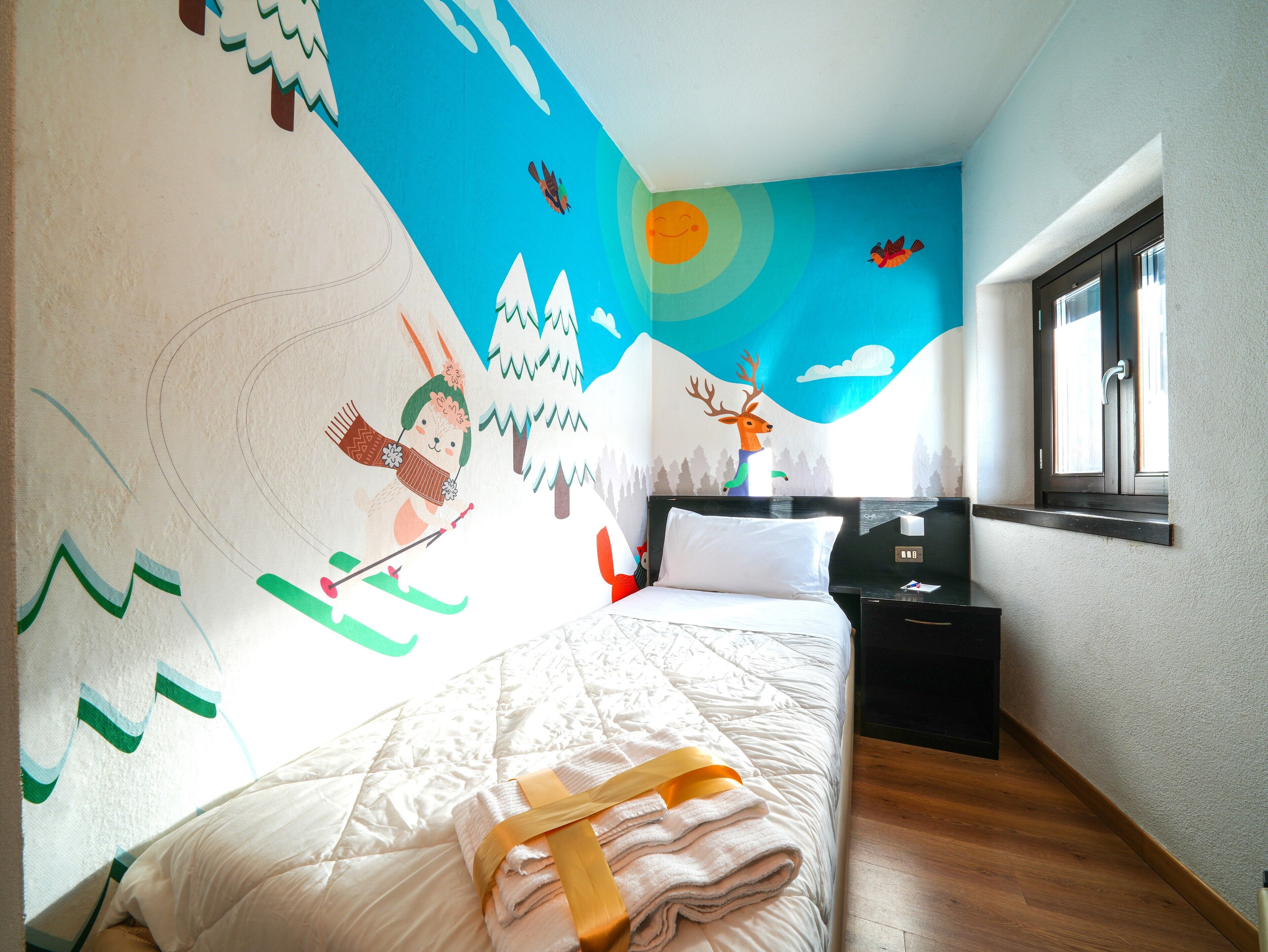 A bedroom with a bed, a nightstand, a window, and a wall mural.