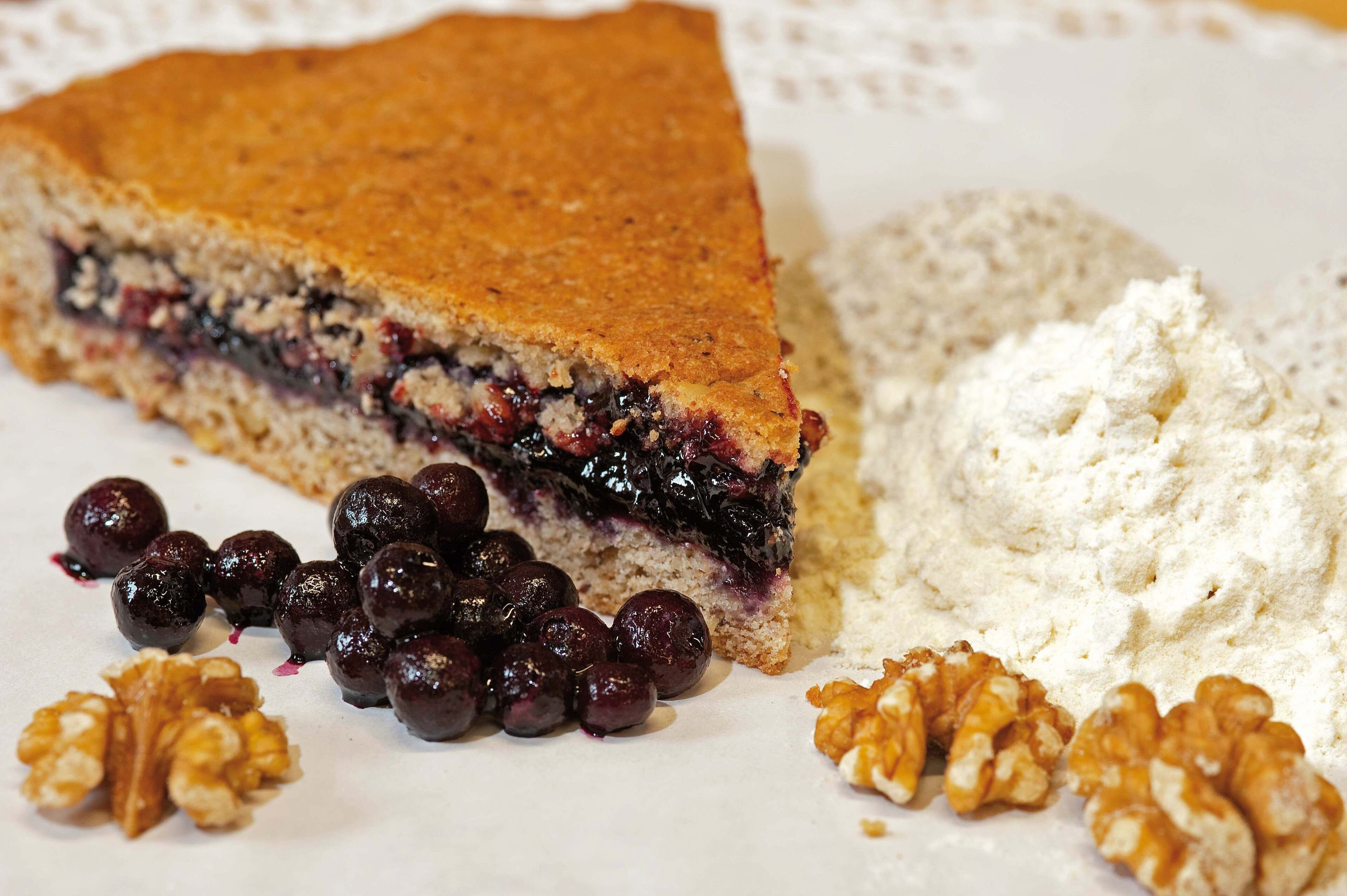 Une part de tarte à la croûte friable et à la garniture aux fruits rouges, servie avec une montagne de sucre glace et des noix.