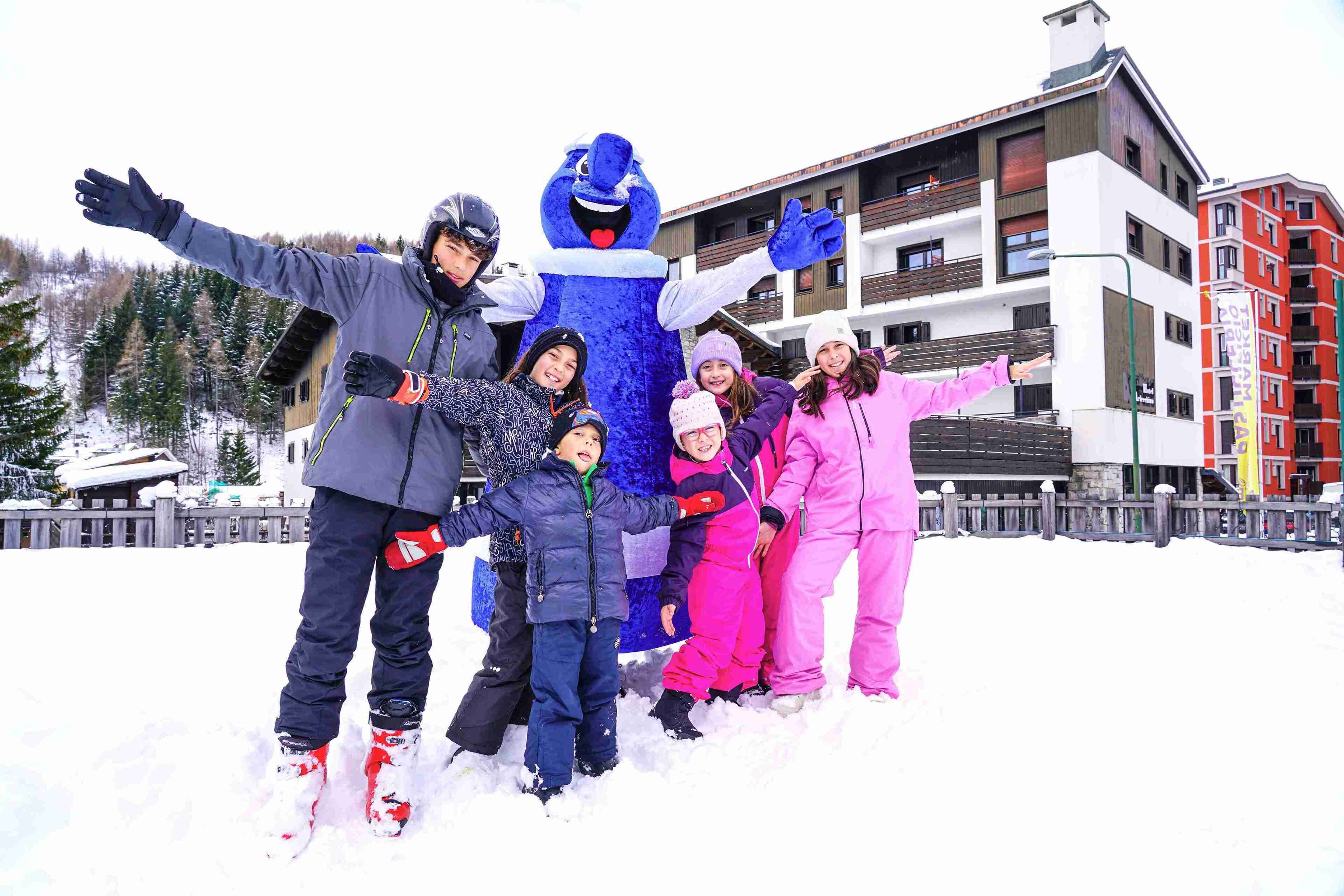 A group of people posing with a mascot in a snowy outdoor setting, with buildings in the background.