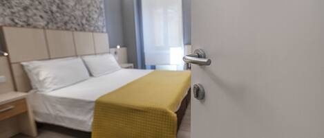 Ein modernes Hotelzimmer mit Bett, Nachttisch und einem fensterbepflanzten Fenster.