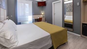 Habitación de hotel con cama, escritorio, silla, televisor y espejo.