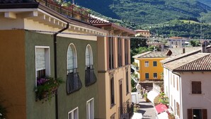 A narrow street with buildings on either side, balconies with plants, and a mountain in the background. - Hotel Aurora (Malcesine)