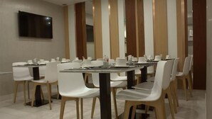 A conference room with white chairs and tables, a flat-screen TV mounted on the wall, and wooden panel dividers. - Hôtel Le Malown (Paris)