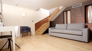 A modern living room with a wooden staircase, a grey sofa, and a white armchair. - Hôtel Le Malown (Paris)