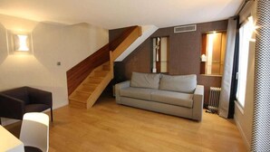 A modern living room with a wooden staircase, a sofa, and a small table. - Hôtel Le Malown (Paris)