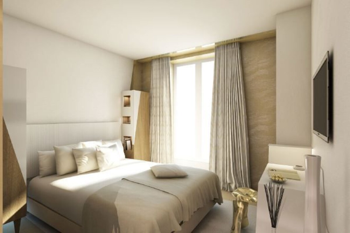 A modern hotel room with a large bed, a bedside table, a TV, and a window with curtains.