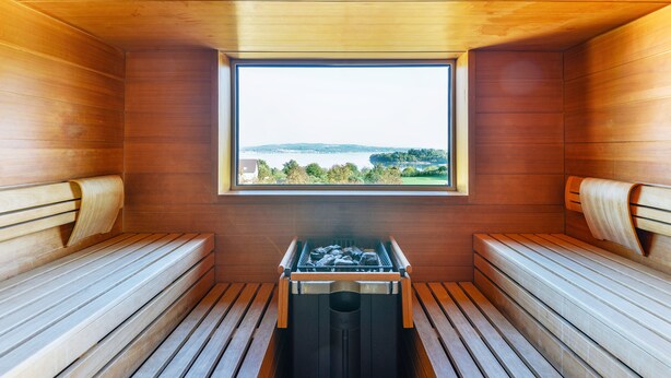 A sauna with wooden benches and a window providing a view of a lake and hills. - Hotel Volapük (Konstanz)
