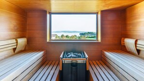 Sauna, jossa on puiset lauteet ja ikkuna, josta avautuu näkymä järvelle ja kukkuloille.