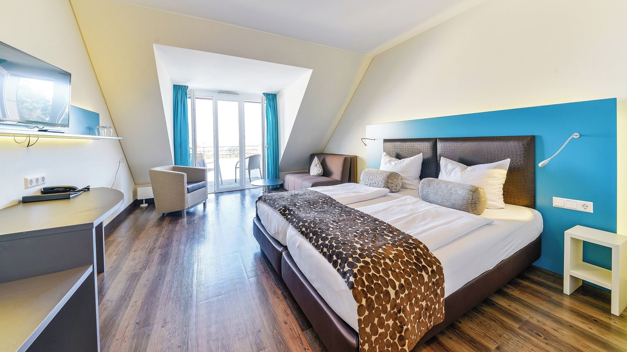 A modern hotel room with a large bed, a desk, and a view of the outdoors.