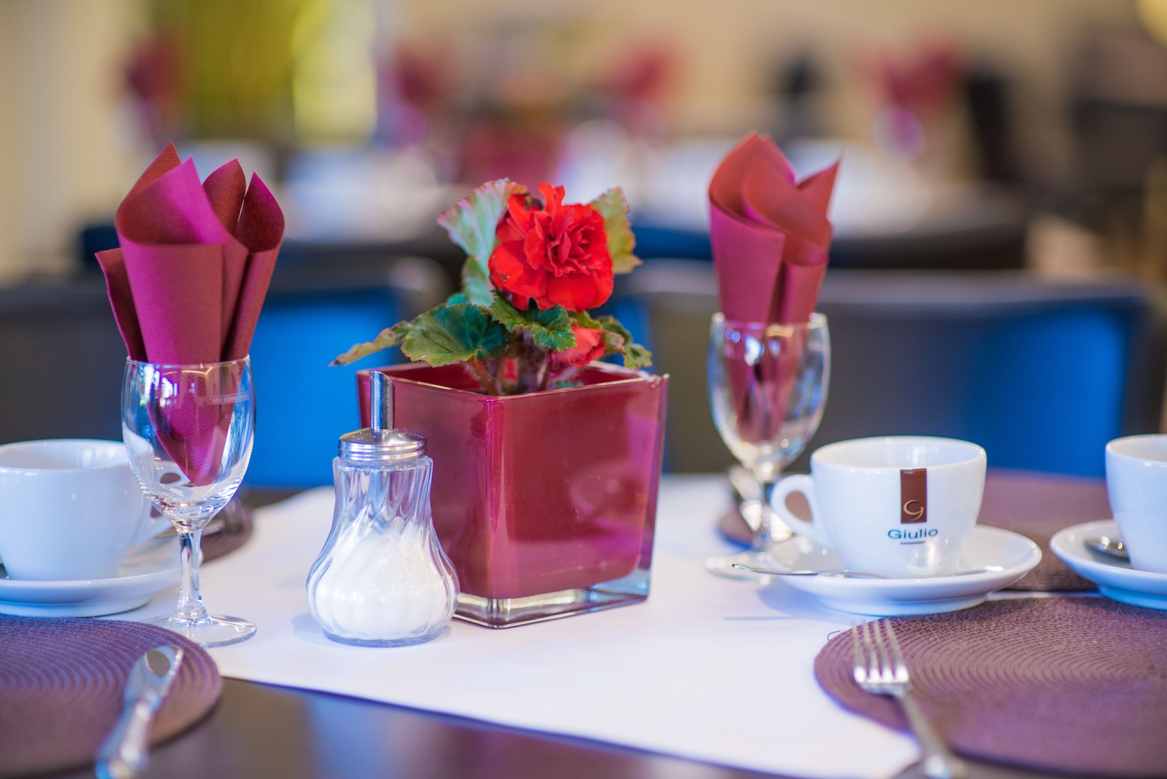 A table set with a red vase, a salt shaker, a white cup with a logo, and a wine glass.