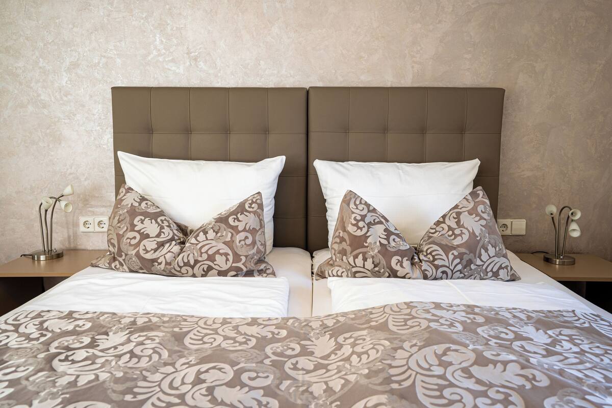 Una cama doble con una colcha estampada, dos almohadas a juego y un cabecero capitonado.