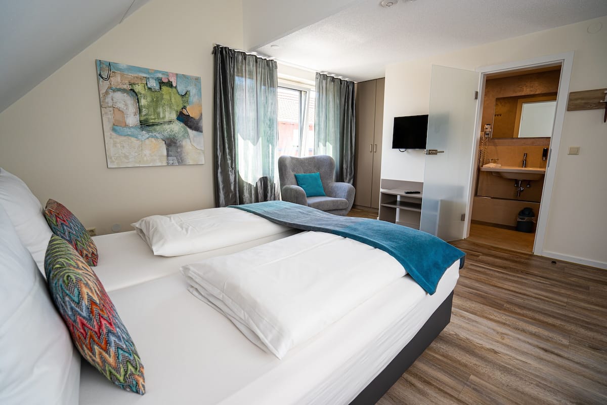 Una habitación de hotel moderna con una cama grande, una silla, un escritorio y un baño visible a través de una puerta abierta.