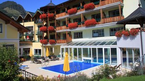 Un hotel con piscina, varios balcones con flores rojas y zona de estar exterior.