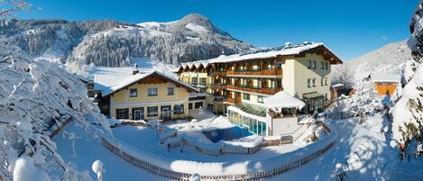 A snow-covered resort with multiple buildings, including a large hotel with balconies and a pool area.