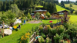 Un entorno rural con una casa de madera, un parque infantil y un jardín cercado.