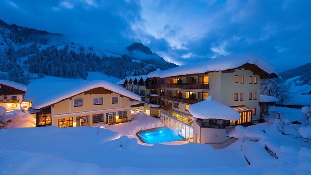 Un hotel grande de varios pisos con piscina, rodeado de nieve, en una zona montañosa.