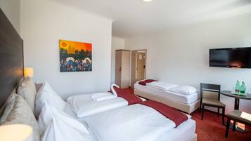 A hotel room with two beds, a TV, a small table with bottles, and a painting on the wall.