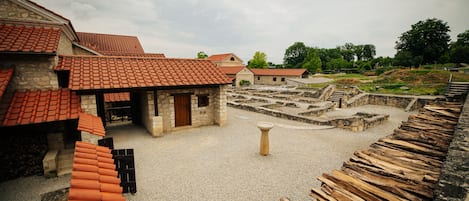 A courtyard with stone buildings and a tiled roof, surrounded by a gravel path and wooden planks.