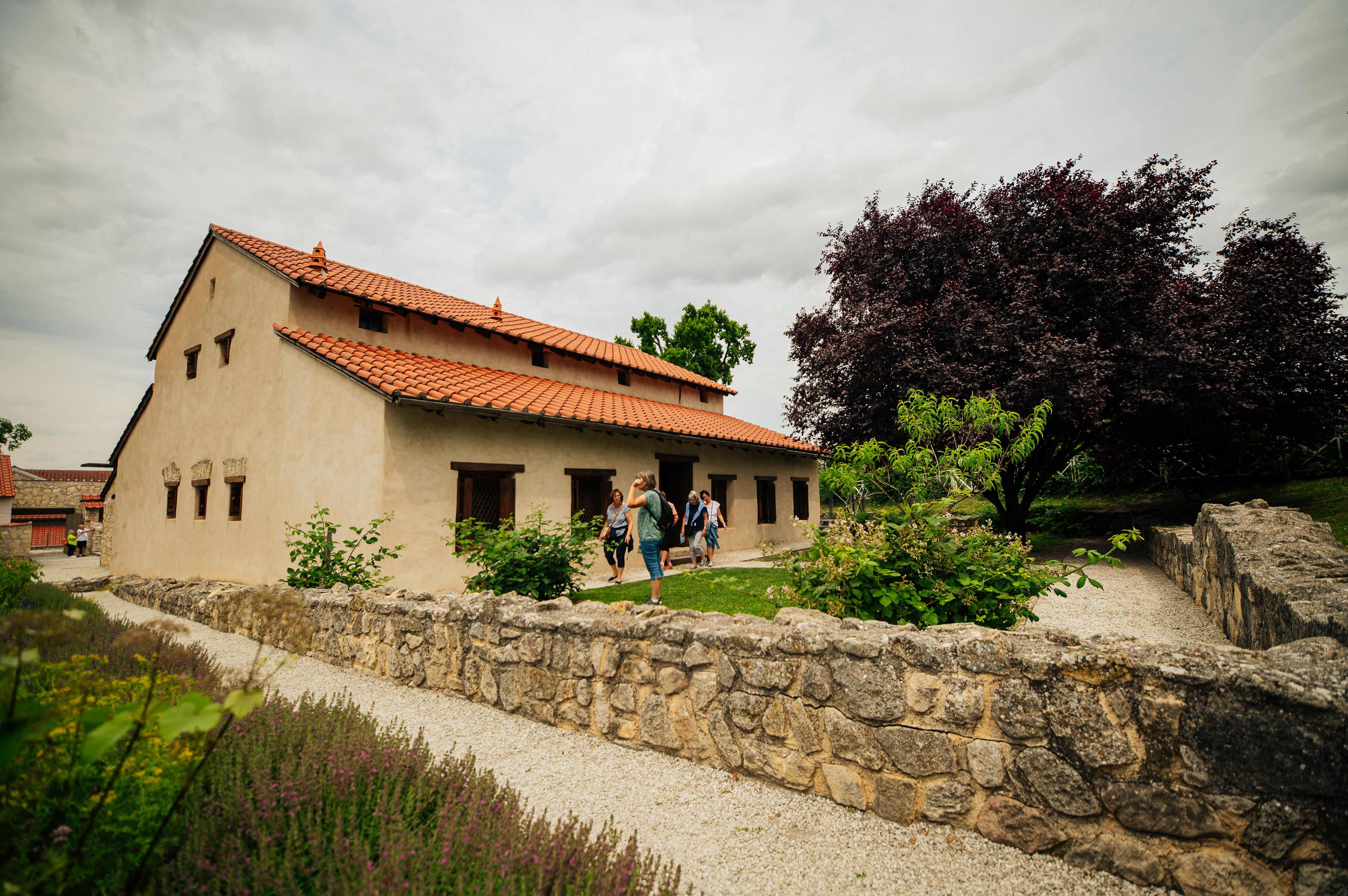 A building with a tiled roof, stone wall, and a pathway leading to it.