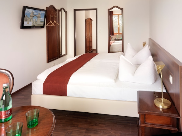 A hotel room with a large bed, a wooden headboard, a bedside table with a lamp, a mirror, and a view of the outside through a window.