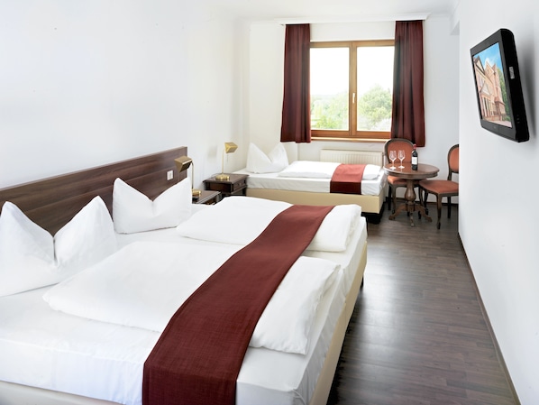 A hotel room with two beds, a dining table with chairs, a TV, and a window with curtains.