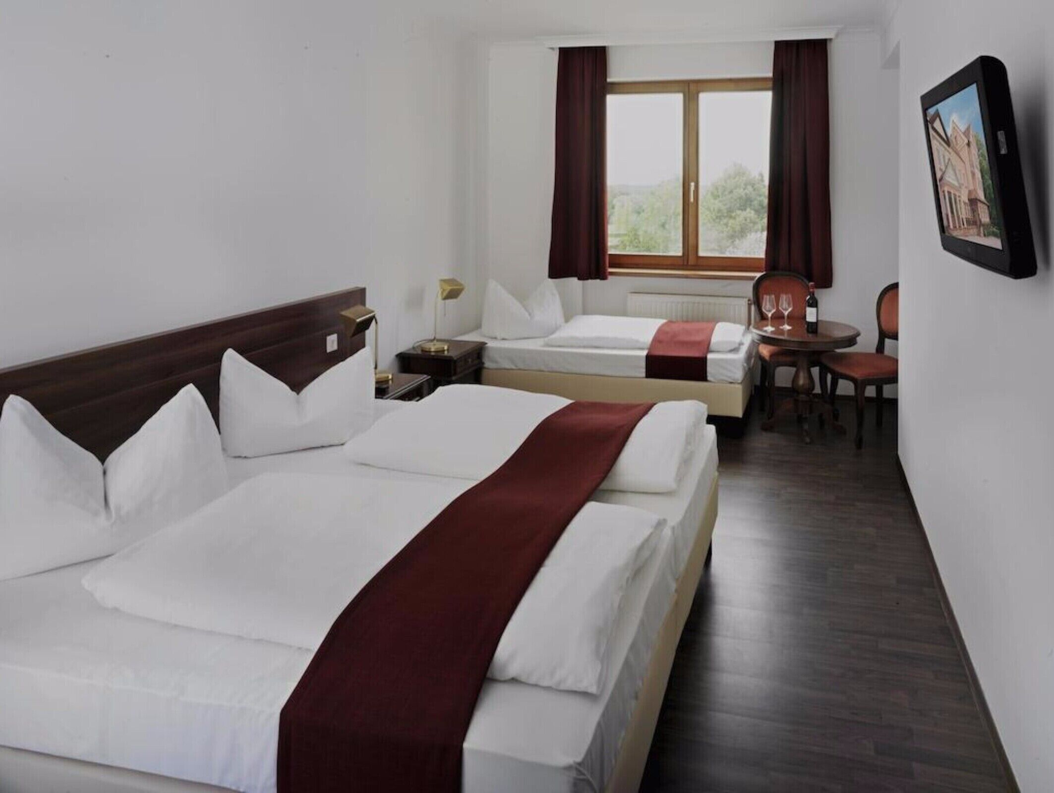 A hotel room with two beds, a dining area, and a window with curtains.