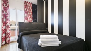 Una habitación de hotel moderna con una cama grande, vistas a través de una puerta corredera y una pared a rayas blancas y negras.