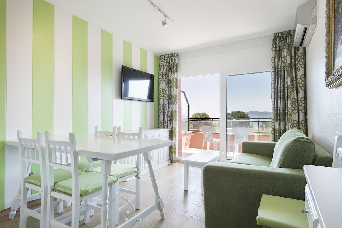 Una habitación con una mesa de comedor, sillas, un sofá, un televisor y un balcón con vistas.