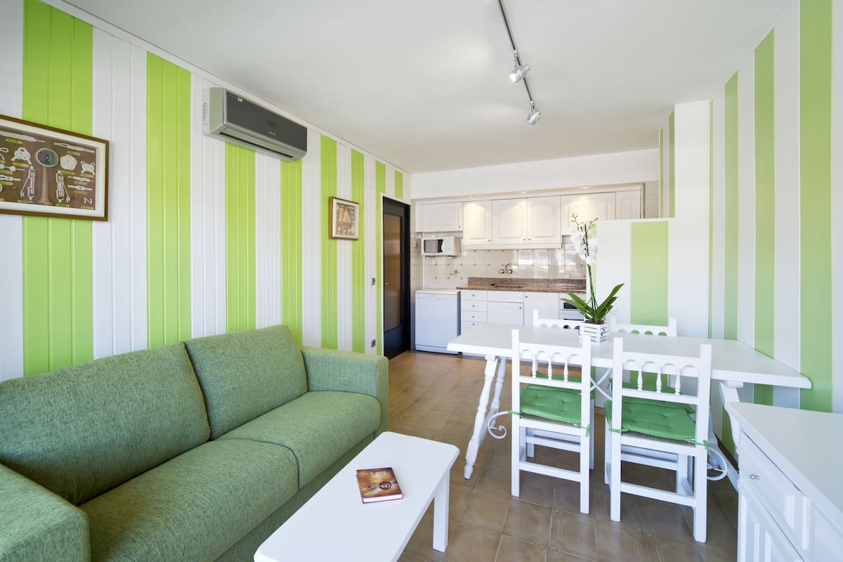Una sala de estar con un sofá verde, una mesa de centro blanca y un comedor con sillas y mesa blancos.