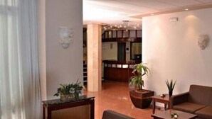 A hotel lobby with a seating area, a reception desk, and a staircase leading to the upper floors. - Primavera (Benidorm)
