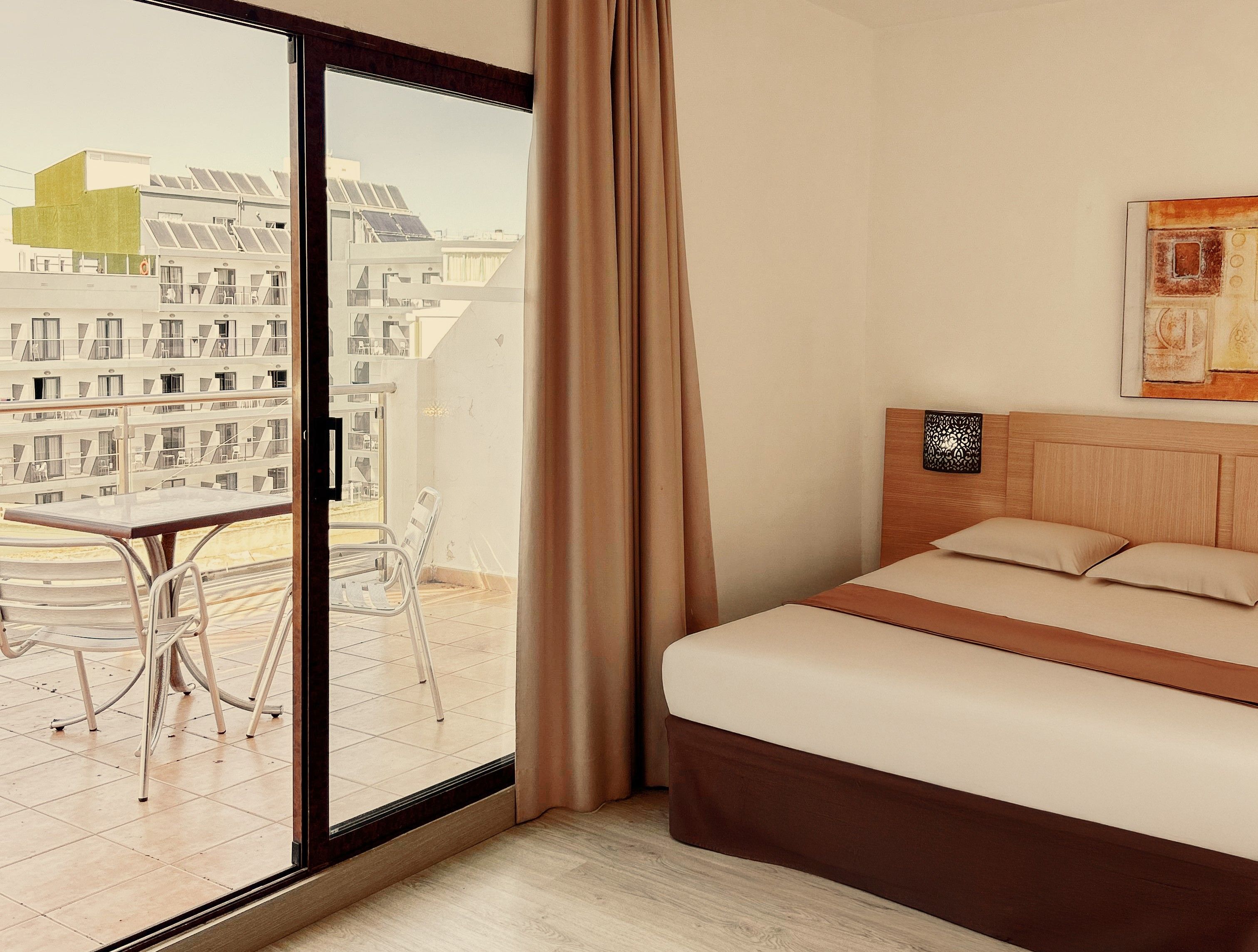 Une chambre d’hôtel avec un lit, une table, des chaises et une vue sur les bâtiments, visible à travers une porte vitrée.