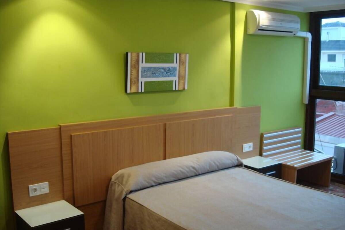 Quarto com cama, mesas de cabeceira, ar-condicionado fixado na parede e janela com vista.
