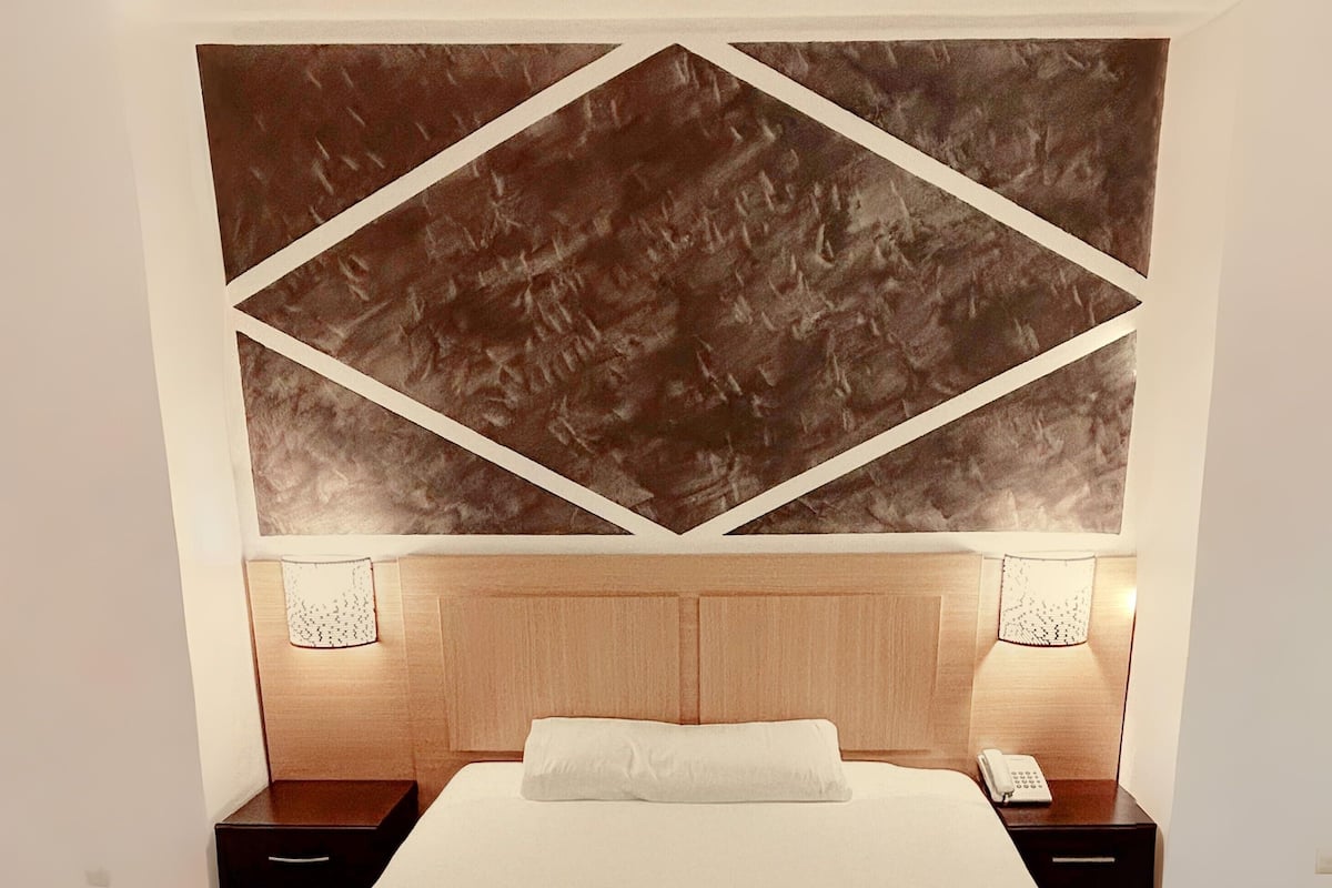 Quarto com uma cama grande, duas mesas de cabeceira, um painel de cama de madeira e duas luminárias fixadas na parede.