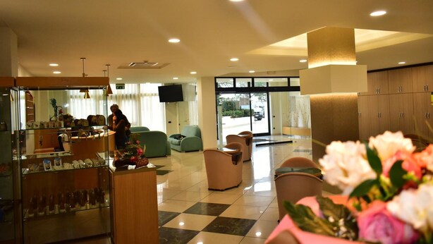 A hotel lobby with a checkered floor, seating area, and a display of items on a counter. - Hotel Garden (San Giovanni Rotondo)