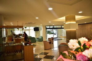 A hotel lobby with a checkered floor, seating area, and a display of items on a counter. - Hotel Garden (San Giovanni Rotondo)