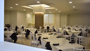 A banquet hall with multiple round tables, white chairs, and a central pillar. - Hotel Garden (San Giovanni Rotondo)