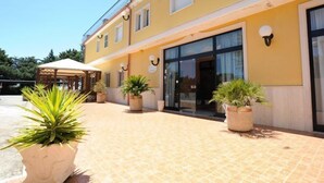 A two-story building with a yellow facade, large windows, and potted plants in the entrance area. - Hotel Garden (San Giovanni Rotondo)