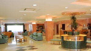 A hotel lobby with a reception desk, seating area, and a large plant. - Hotel Garden (San Giovanni Rotondo)